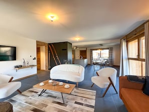 A spacious living area with a sofa, chairs, a coffee table, and a television mounted on the wall.