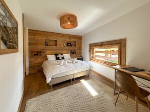 Een slaapkamer met een houten hoofdeinde, een bed met witte beddengoed, een bureau met stoel en een raam met uitzicht.