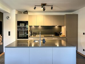 Cozinha moderna com ilha central, eletrodomésticos de aço inoxidável e iluminação embutida.
