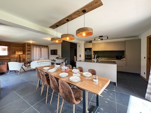 A modern kitchen with a central island, dining area with a wooden table and chairs, and a cozy seating area with a fireplace.