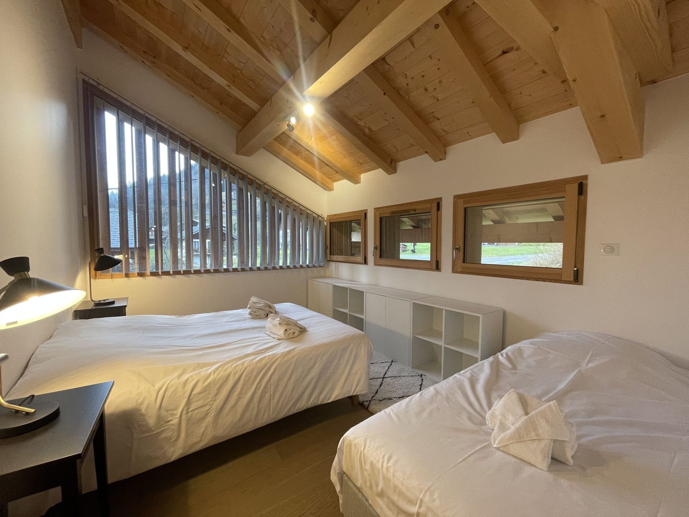 A bedroom with two beds, a desk, a lamp, and a window with blinds.