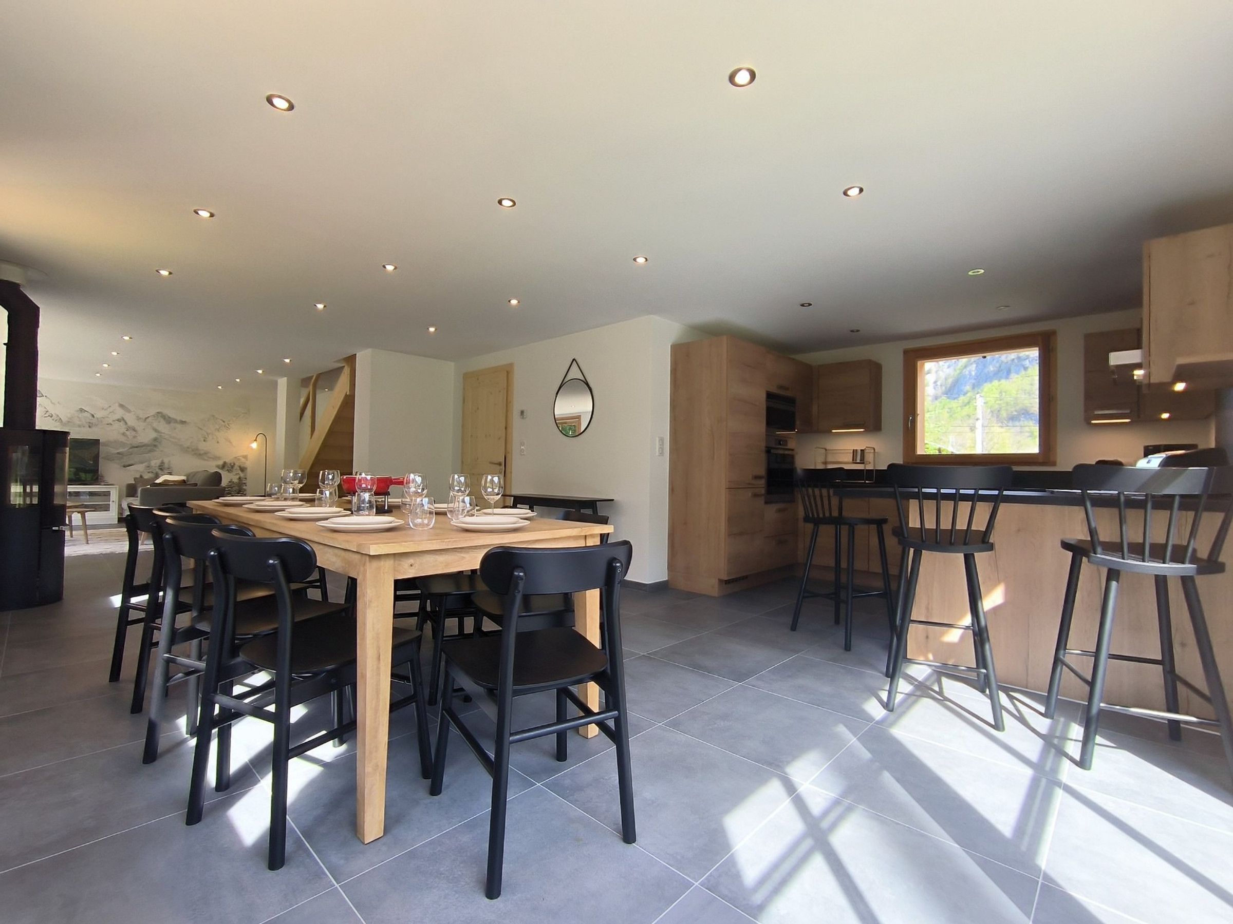 Una cocina moderna con armarios de madera, un comedor con mesa y sillas de madera, y un amplio ventanal que proporciona luz natural.
