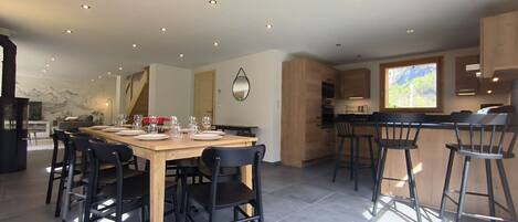 Una cocina moderna con armarios de madera, un comedor con mesa y sillas de madera, y un amplio ventanal que proporciona luz natural.