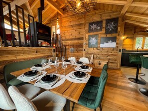 Ein Holzinterieur mit einem Esstisch, der für sechs Personen gedeckt ist, einem Kamin und einer Küchenzeile.