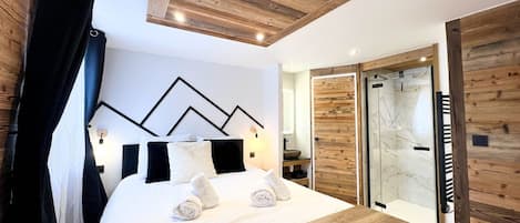 A modern bedroom with a wooden headboard, a bed with white bedding, a wooden bedside table, and a glass shower enclosure.