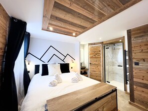Ein modernes Schlafzimmer mit einem Holzkopfteil, einem Bett mit weißer Bettwäsche, einem Nachttisch aus Holz und einer Duschkabine aus Glas.