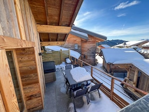 Eine Holzhütte mit Balkon, Sitzgelegenheiten im Freien und verschneiter Umgebung.