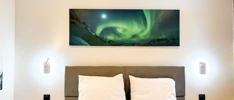 A bedroom with a bed, two bedside tables, and a painting of the Northern Lights on the wall.