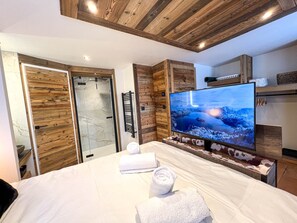 A modern hotel room with a large bed, a television, and a glass shower enclosure. - Luxury Chalet in Les Gets - 4 Bedrooms for 9 Guests with Jacuzzi and Wi-Fi (Les Gets)