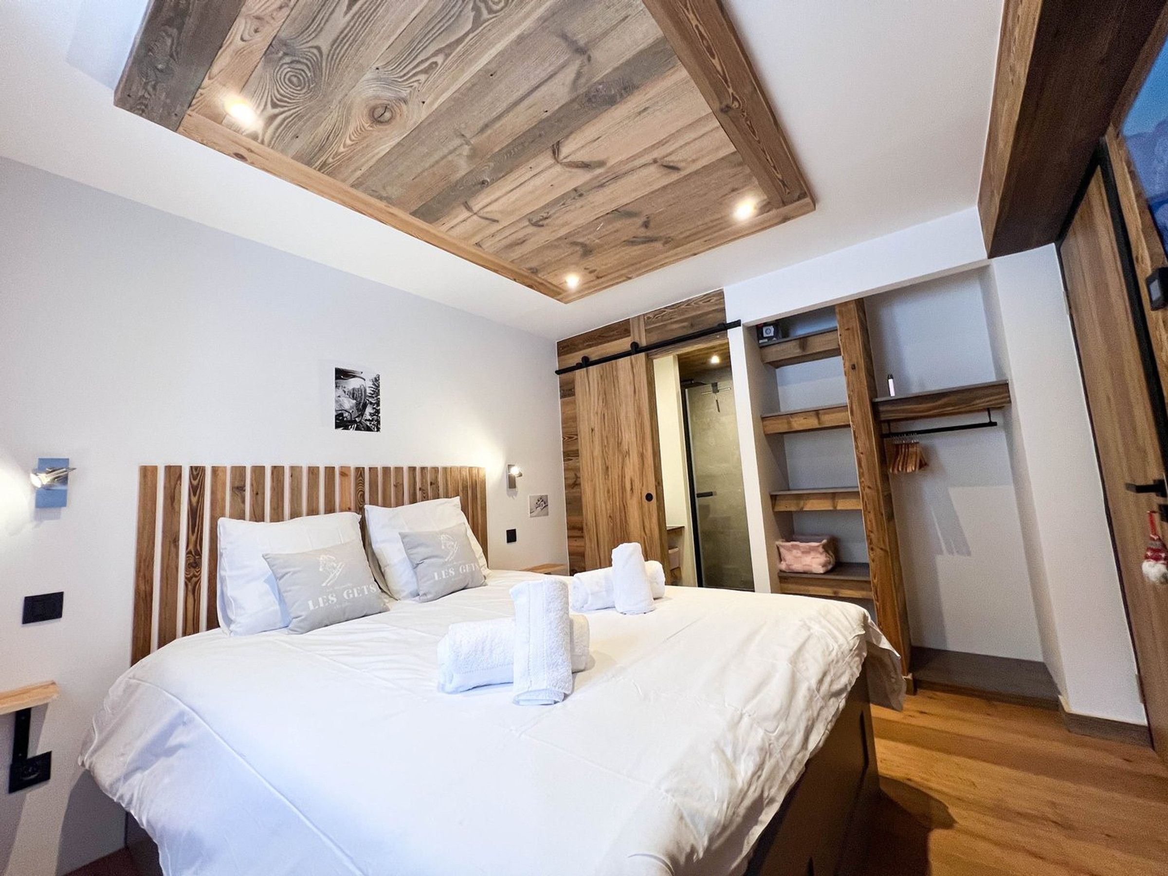 A hotel room with a wooden ceiling, a bed with white bedding, and a walk-in closet with wooden shelves.