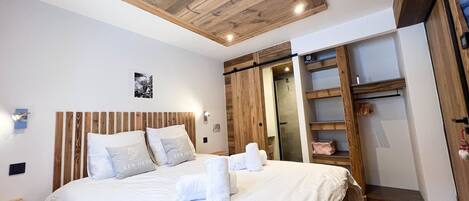 A hotel room with a wooden ceiling, a bed with white bedding, and a walk-in closet with wooden shelves.