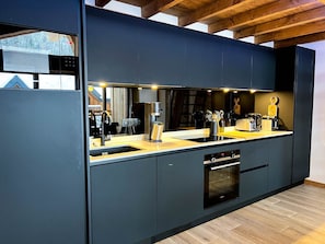 A modern kitchen with dark cabinetry, a double sink, and a built-in oven. - Apartment in Les Gets - 2 bedrooms, 6 guests, Private garage (Les Gets)