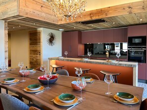 Eine moderne Küche mit Holzschnitzereien, einer zentralen Kochinsel und einem Essbereich mit einem langen Tisch, gedeckt für eine Mahlzeit.