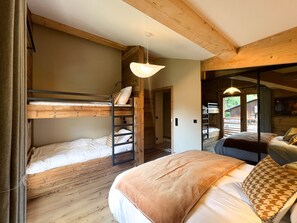 Ein Zimmer mit einem Etagenbett, einem Einzelbett und einer Holzbalkendecke.