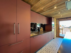 Eine moderne Küche mit Holzboden und roten Schränken, einem Spülbecken und Blick ins Freie.