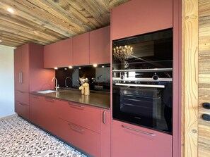 Eine moderne Küche mit roten Schränken, einem Edelstahlbackofen und einer Holzbalkendecke.