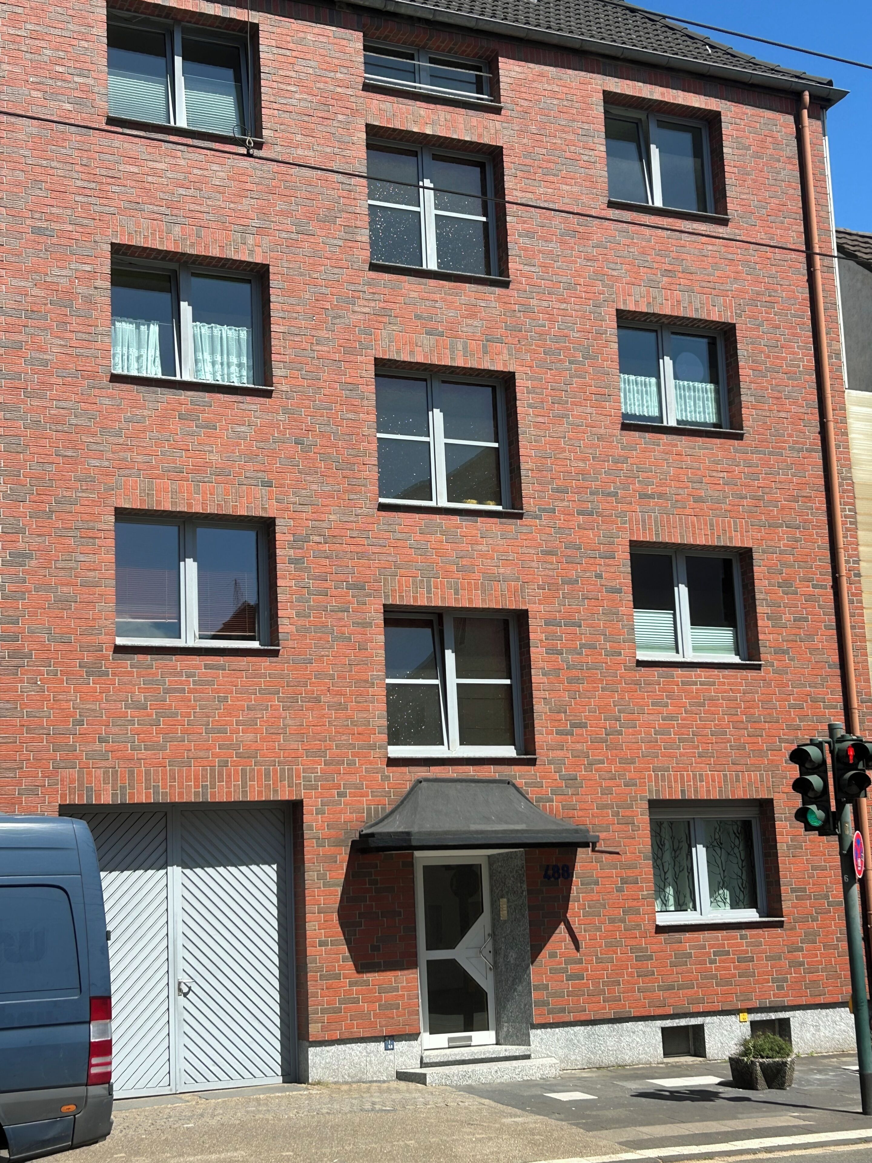 Ein mehrstöckiges Backsteingebäude mit Garagentor, überdachter Eingangspartei und einer Ampel.