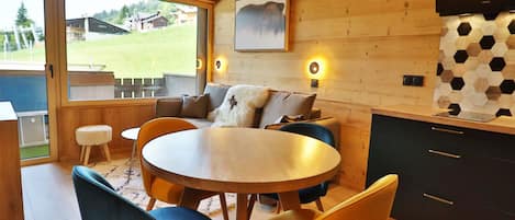 Un acogedor interior de cabaña con una mesa redonda de comedor, sillas de madera, un sofá y un televisor montado en la pared.