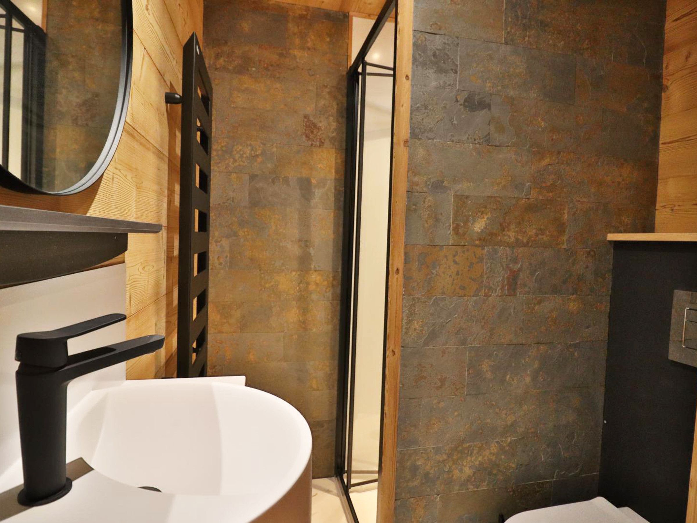 Une salle de bain avec un lavabo blanc, un miroir et un mur en pierre.