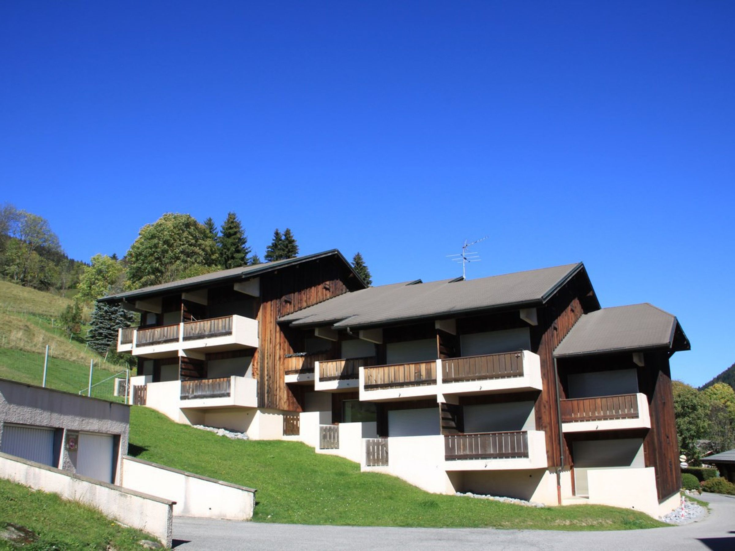 A multi-story building with balconies, set on a hillside with a clear sky.