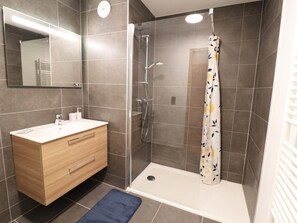 A modern bathroom with a glass-enclosed shower, a wooden vanity with a sink, and a blue bath mat. - Comfortable apartment - 4 guests (Les Gets)