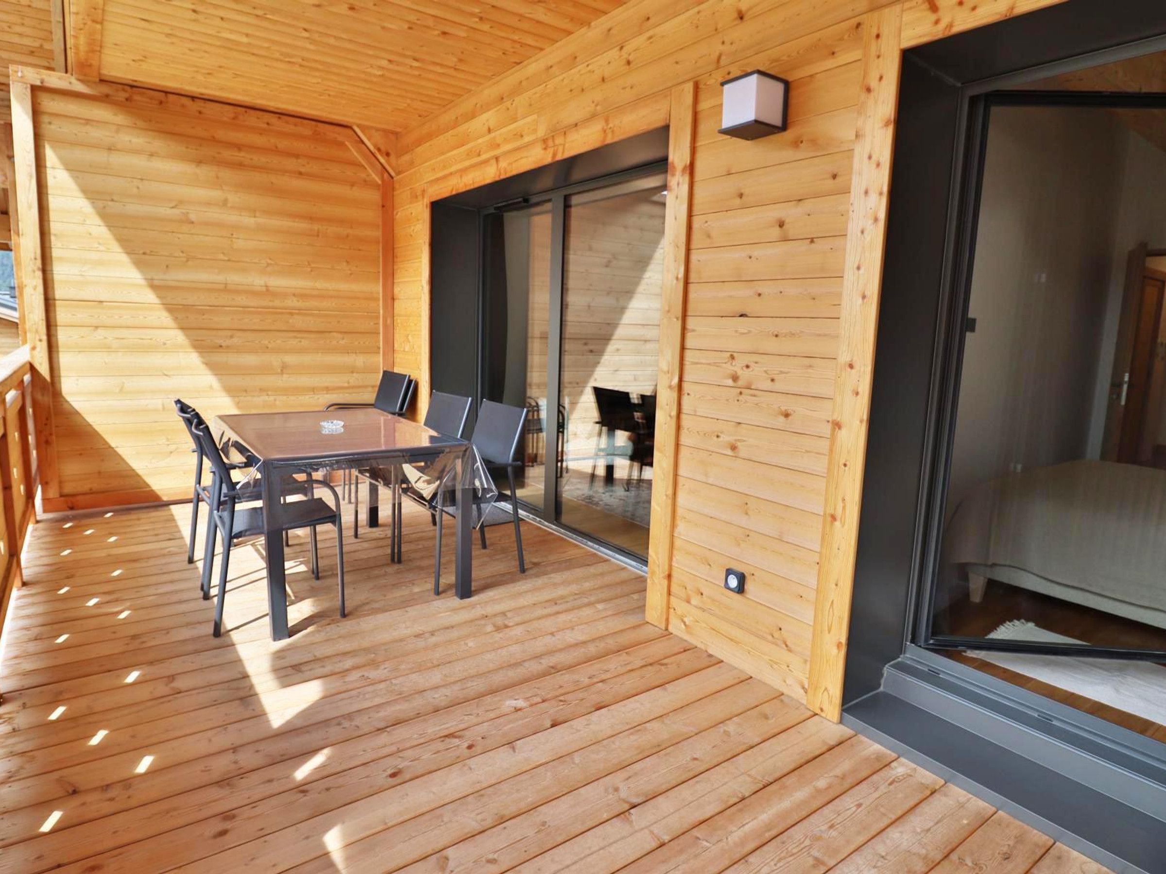 Une terrasse en bois avec une table et des chaises, une porte-fenêtre coulissante et un petit luminaire.