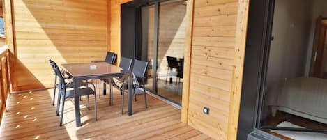 Une terrasse en bois avec une table et des chaises, une porte-fenêtre coulissante et un petit luminaire.