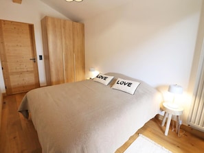 A bedroom with a bed, two pillows with the word 'LOVE,' a nightstand with a lamp, a wooden wardrobe, and a door. - Comfortable apartment - 4 guests (Les Gets)