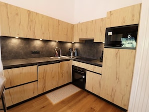 A modern kitchen with wooden cabinetry, a black countertop, and a built-in oven. - Comfortable apartment - 4 guests (Les Gets)