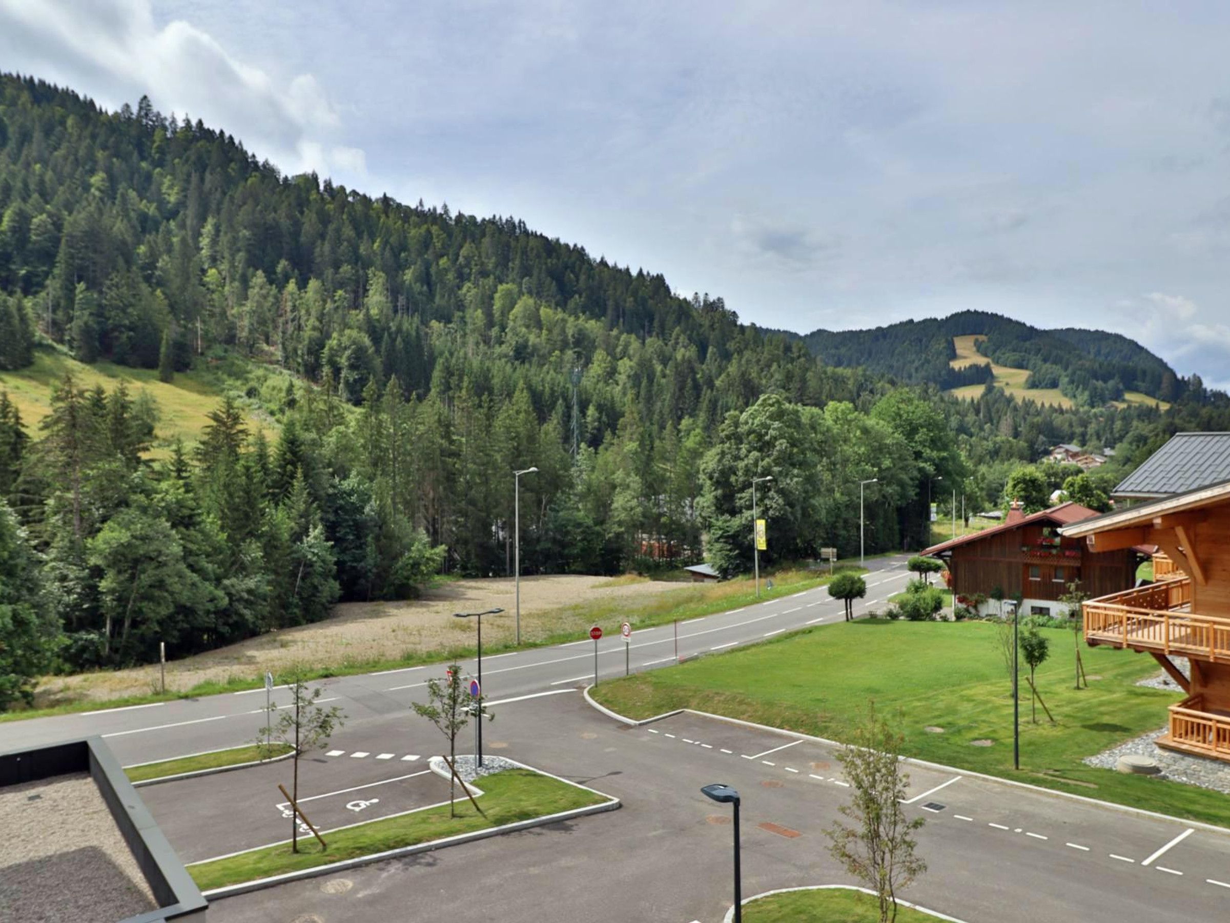 A road intersection with a pedestrian crossing, surrounded by a forested mountain backdrop.
