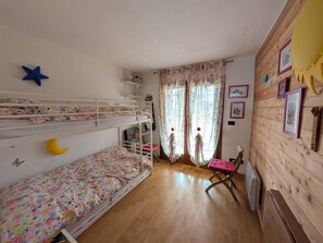 Una habitación con literas, una silla, un radiador y una ventana con cortinas.