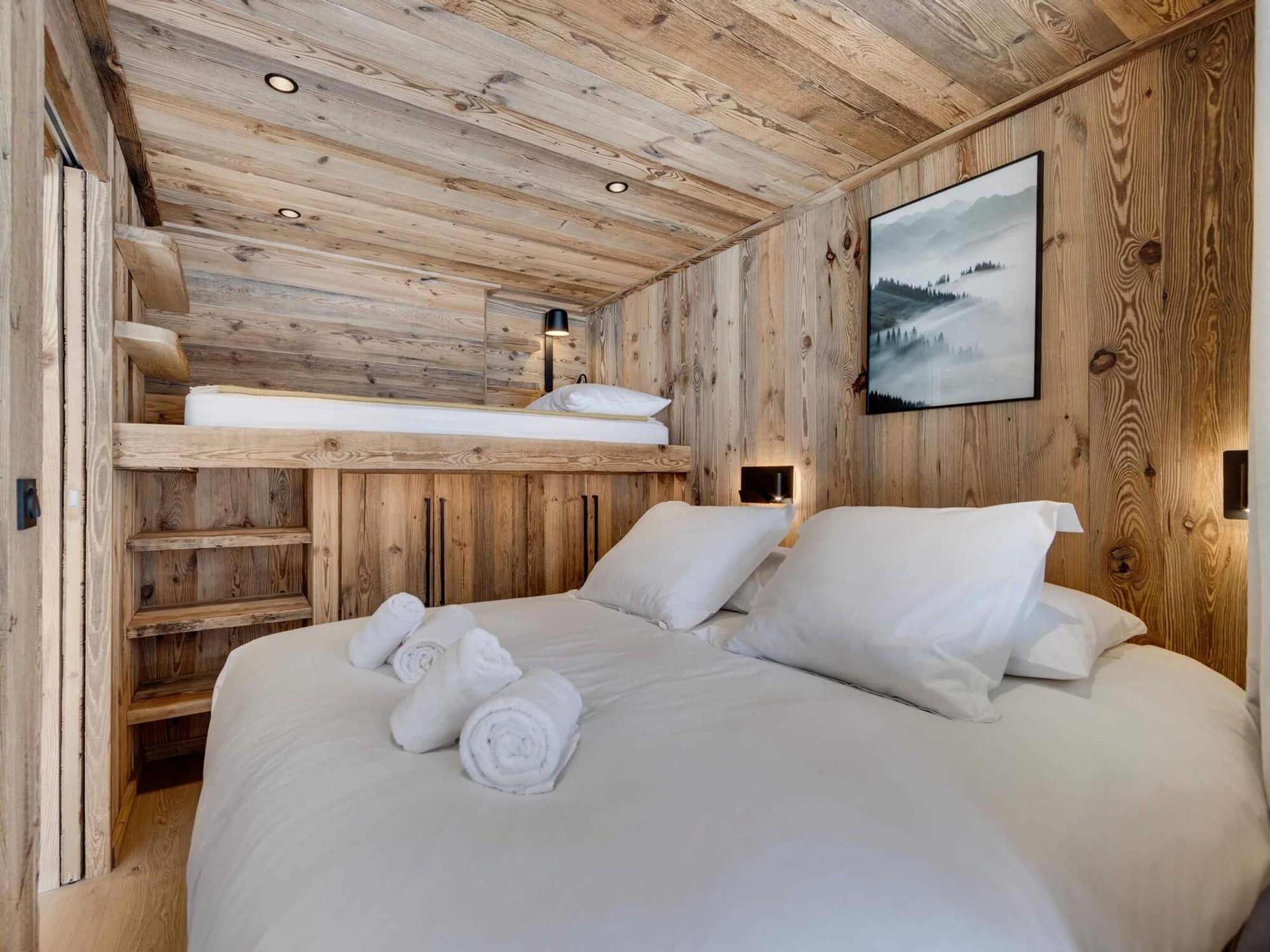 A wooden cabin bedroom with a bunk bed, a large bed, and a framed picture on the wall.