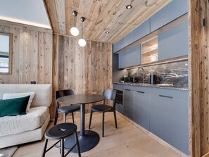 A compact kitchen with wooden walls, a dining area with a round table and chairs, and a sofa with a green pillow. - Renovated apartment at the foot of the slopes - 2 guests (Val-d'Isère)