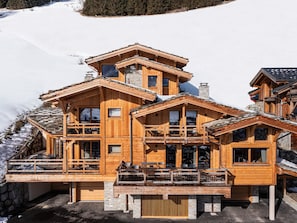 A multi-story wooden chalet with balconies, set against a snowy backdrop. - Exceptional apartment, mountain view - 10 guests (Les Deux Alpes)