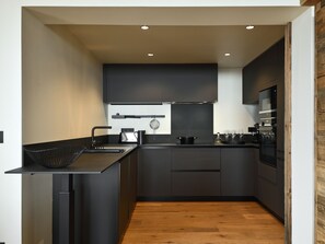 A modern kitchen with dark cabinetry, a wooden countertop, and a built-in oven. - Exceptional apartment, mountain view - 10 guests (Les Deux Alpes)
