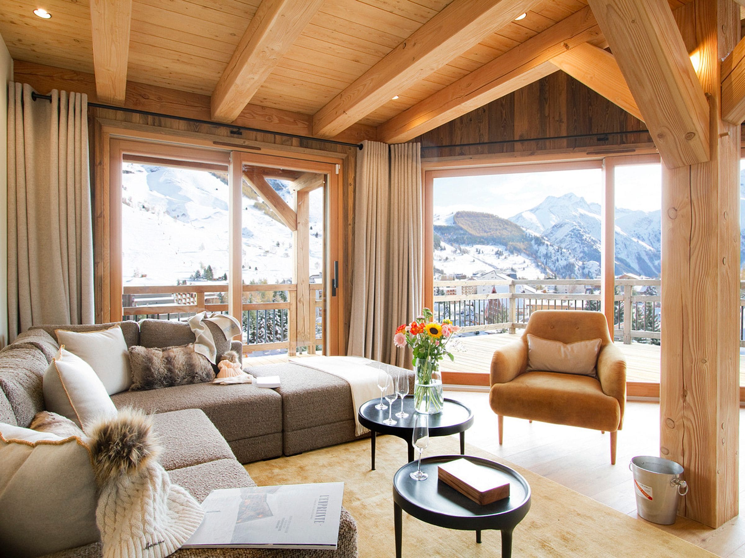 Un salon chaleureux avec un canapé, un fauteuil et une table basse, agrémenté d’une grande fenêtre offrant une vue sur les montagnes.
