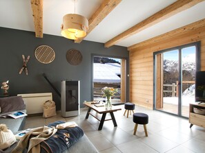 A modern living room with a fireplace, a sofa, a dining table with chairs, and a large window offering a mountain view. - Spacious chalet mountain view - 10 guests (Les Deux Alpes)