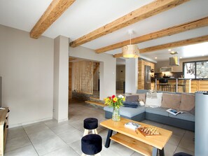 A modern living room with a wooden ceiling, a sofa, a coffee table with a chess set, and a vase with flowers. - Spacious chalet mountain view - 10 guests (Les Deux Alpes)