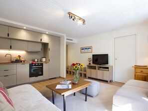 A modern living room with a wooden coffee table, a sofa, a TV, and a kitchen area with a stove and cabinets. - Charming apartment at foot of slopes - 6 guests (Les Deux Alpes)