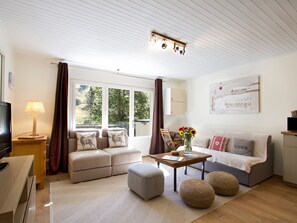A modern living room with a sofa, ottomans, a coffee table, and a television. - Charming apartment at foot of slopes - 6 guests (Les Deux Alpes)