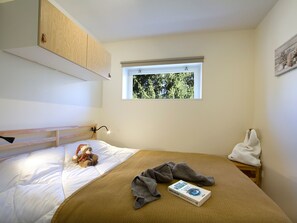 Ein Schlafzimmer mit Etagenbett, einem Fenster mit Blick auf Bäume, einer Nachttischlampe und einem Buch auf dem Bett.