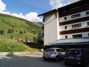 A building with a parking area, two cars parked, and a mountainous landscape in the background. - Central T1 loft with parking - 4 guests (Les Deux Alpes)