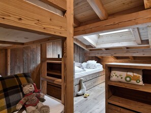 Ein gemütliches Holzschlafzimmer mit einem Schlafplatz auf dem Hochbett, einem kuscheligen Teddybären und einem Kissen mit Traktormotiv.