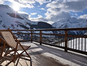 Eine Holzterrasse mit einem Stuhl, mit Blick auf eine verschneite Berglandschaft.