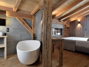 Ein modernes Interieur mit einer großen Badewanne, Holzbalken, Steinwänden und einer gemütlichen Sitzecke.