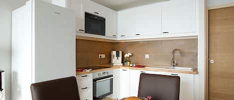 Una cocina compacta con armarios blancos, un microondas, horno y un lavamanos.