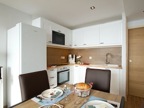 A compact kitchen with white cabinets, a microwave, oven, and a sink. - Apartment with view of La Muzelle - 4 guests (Les Deux Alpes)