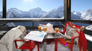 Ein Tisch mit einer Speisekarte, einem Glas Orangensaft und einer Saftflasche vor einer verschneiten Bergkulisse.