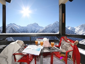 A table with a menu, a glass of orange juice, and a bottle of juice, set against a snowy mountain backdrop. - Apartment with view of La Muzelle - 4 guests (Les Deux Alpes)