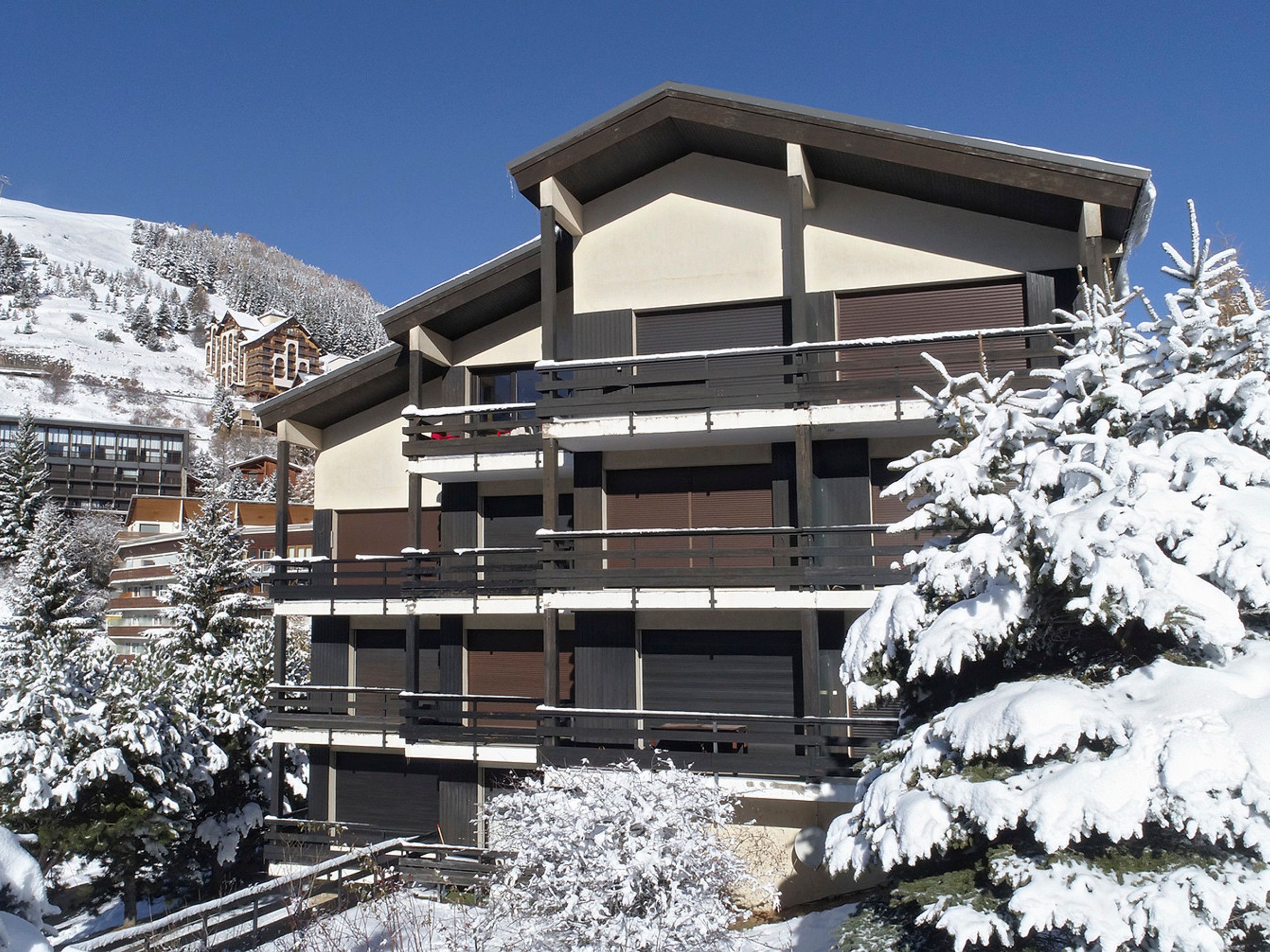 A multi-story building with balconies, surrounded by snow-covered trees.